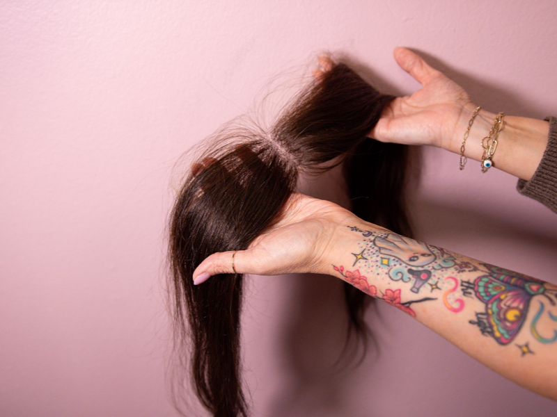 Person with tattoos styling hair against a pink background