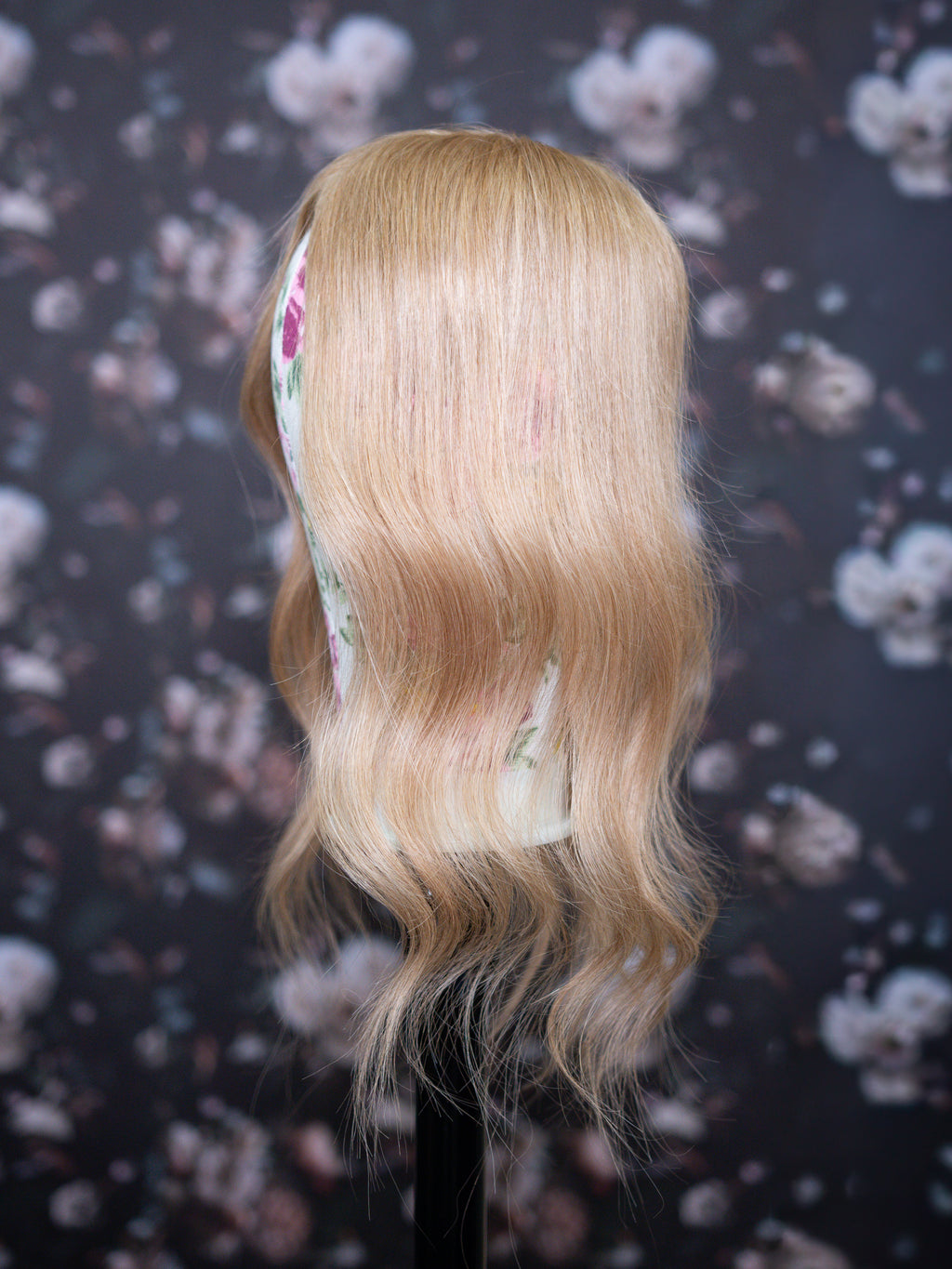 Blonde wig on a mannequin head with a floral-patterned background