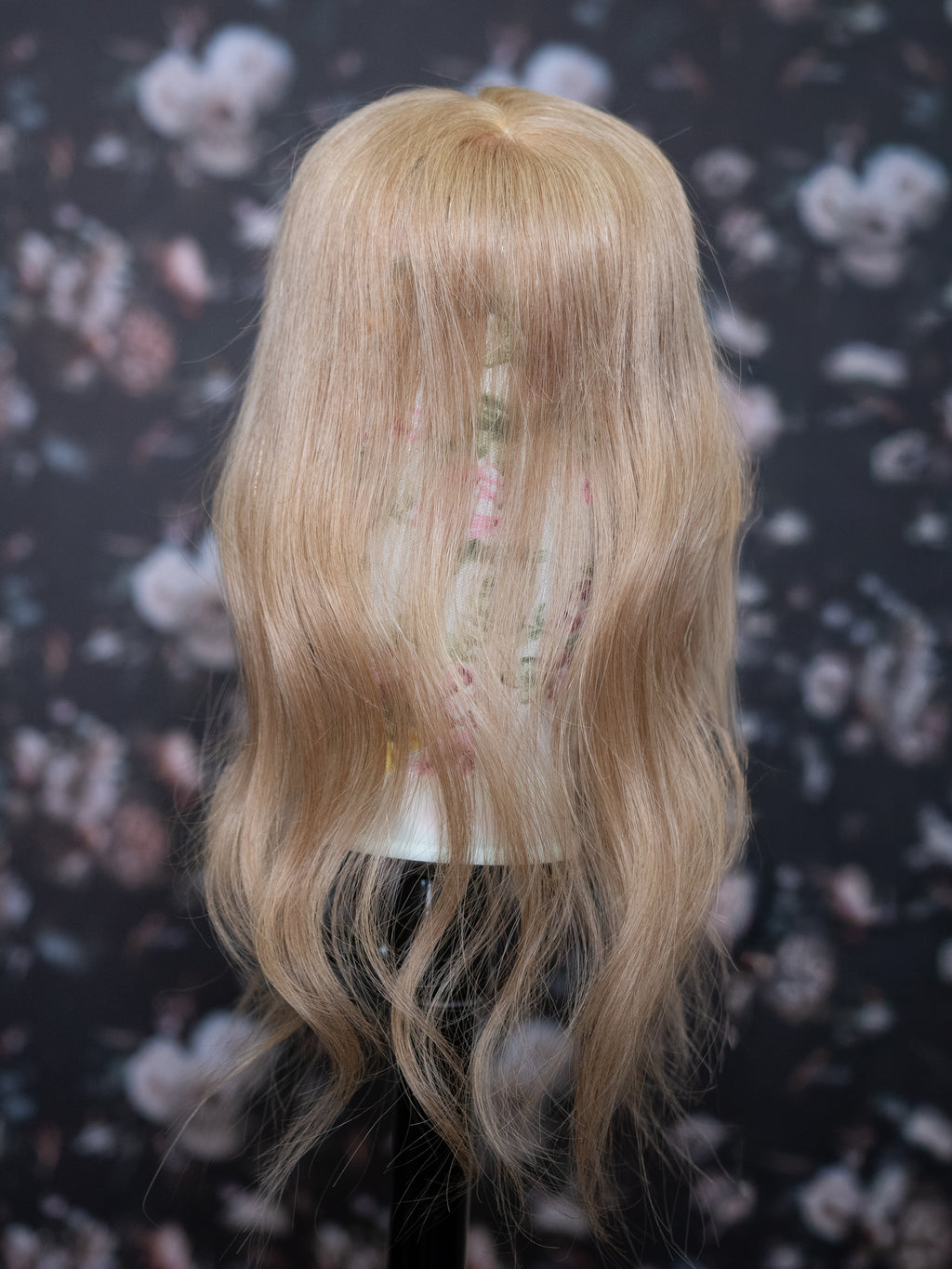 Blonde wig on a mannequin head against a floral patterned background