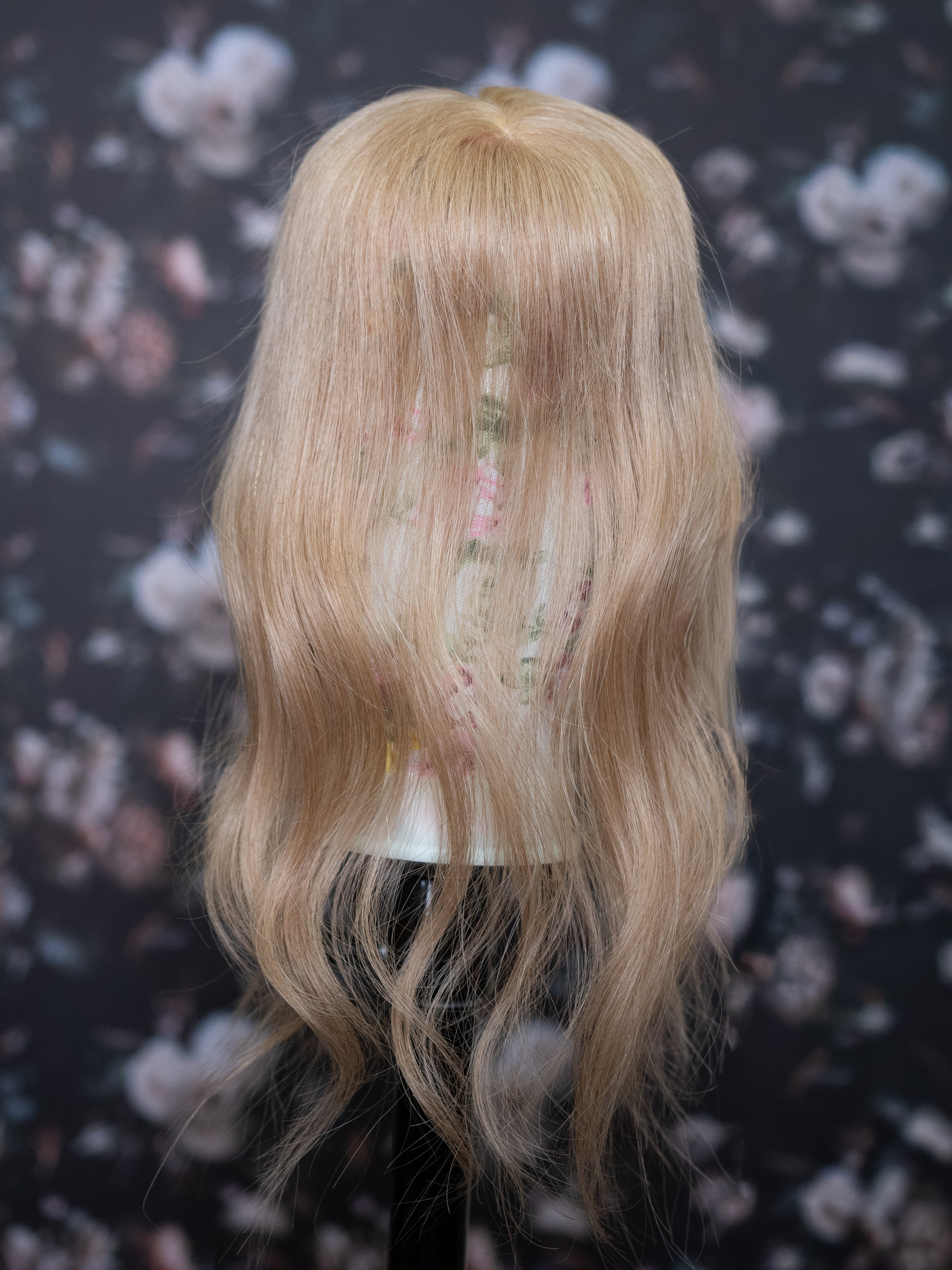 Blonde wig on a mannequin head against a floral patterned background