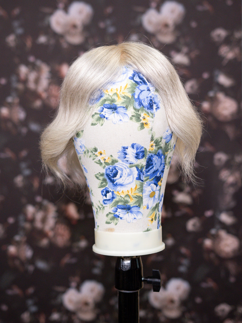 Mannequin head with blonde wig and floral-patterned headband against a floral background