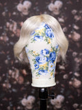 Mannequin head with blonde wig and floral-patterned headband against a floral background