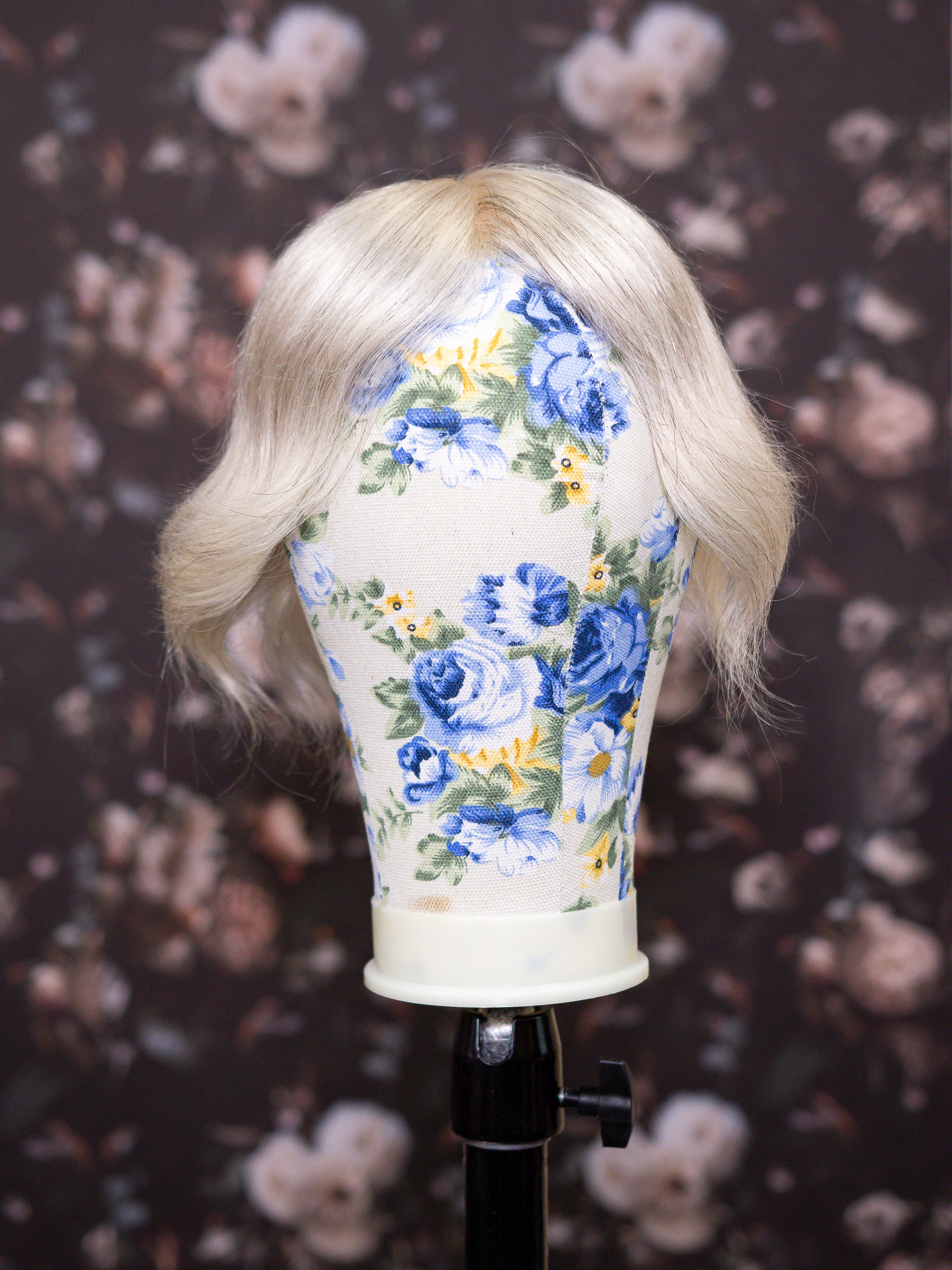 Mannequin head with blonde wig and floral-patterned headband against a floral background