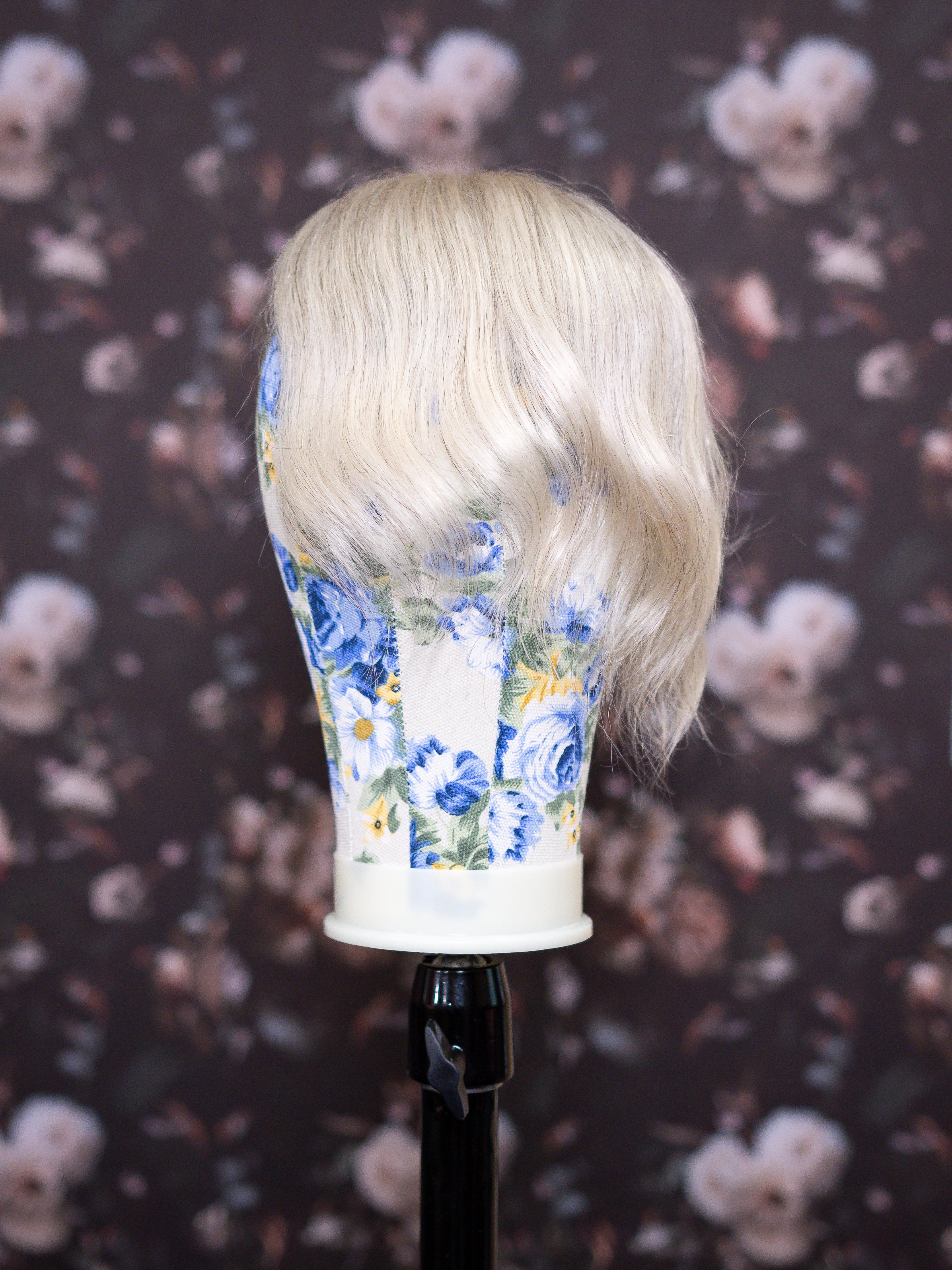 Blonde wig on a floral-patterned mannequin head against a dark floral background