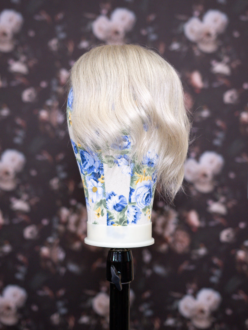 Blonde wig on a floral-patterned mannequin head against a dark floral background