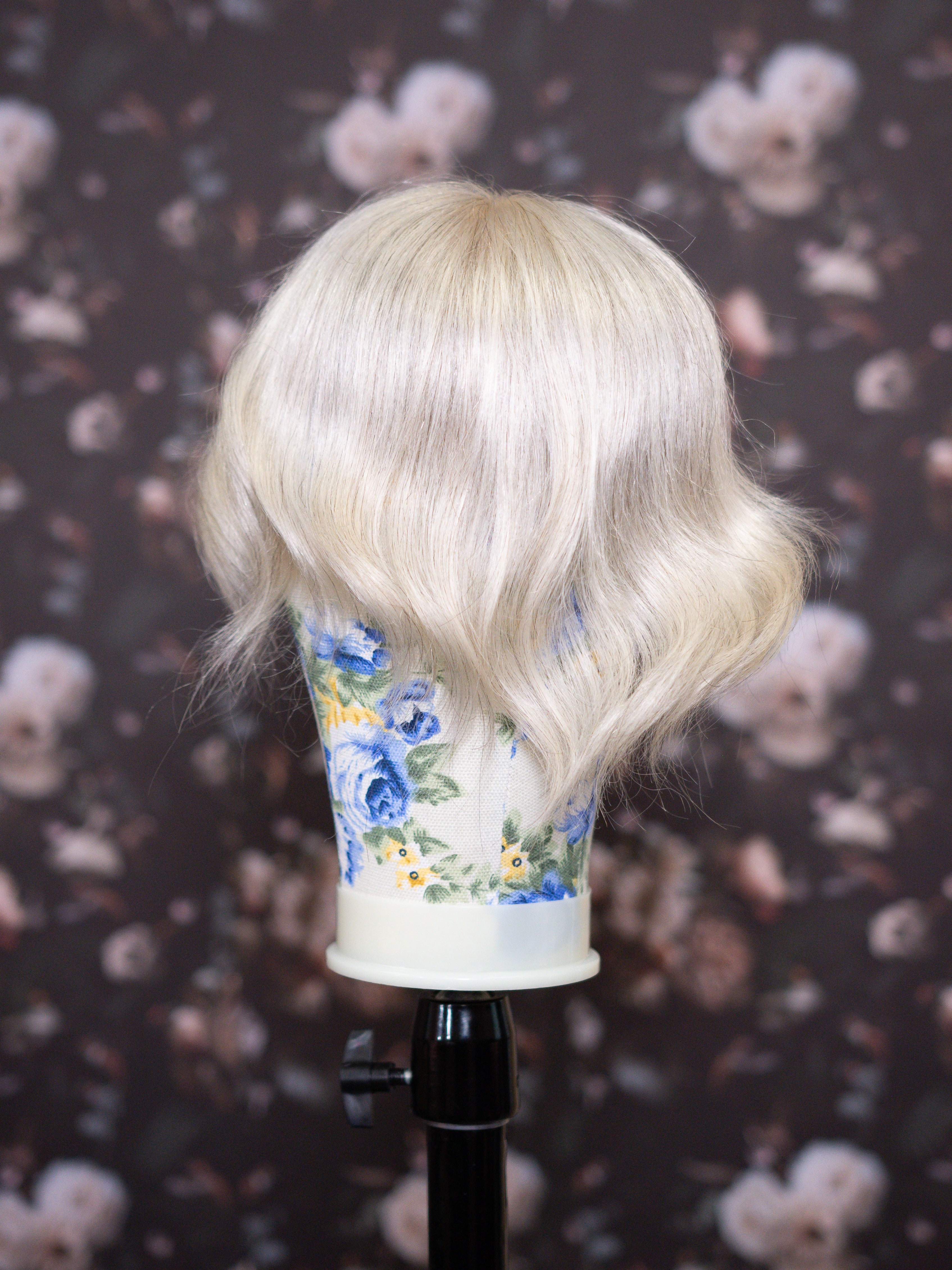 Blonde wig on a mannequin head with a floral-patterned cup against a dark floral background
