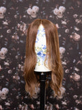 Brown wig on a mannequin head against a floral wallpaper background