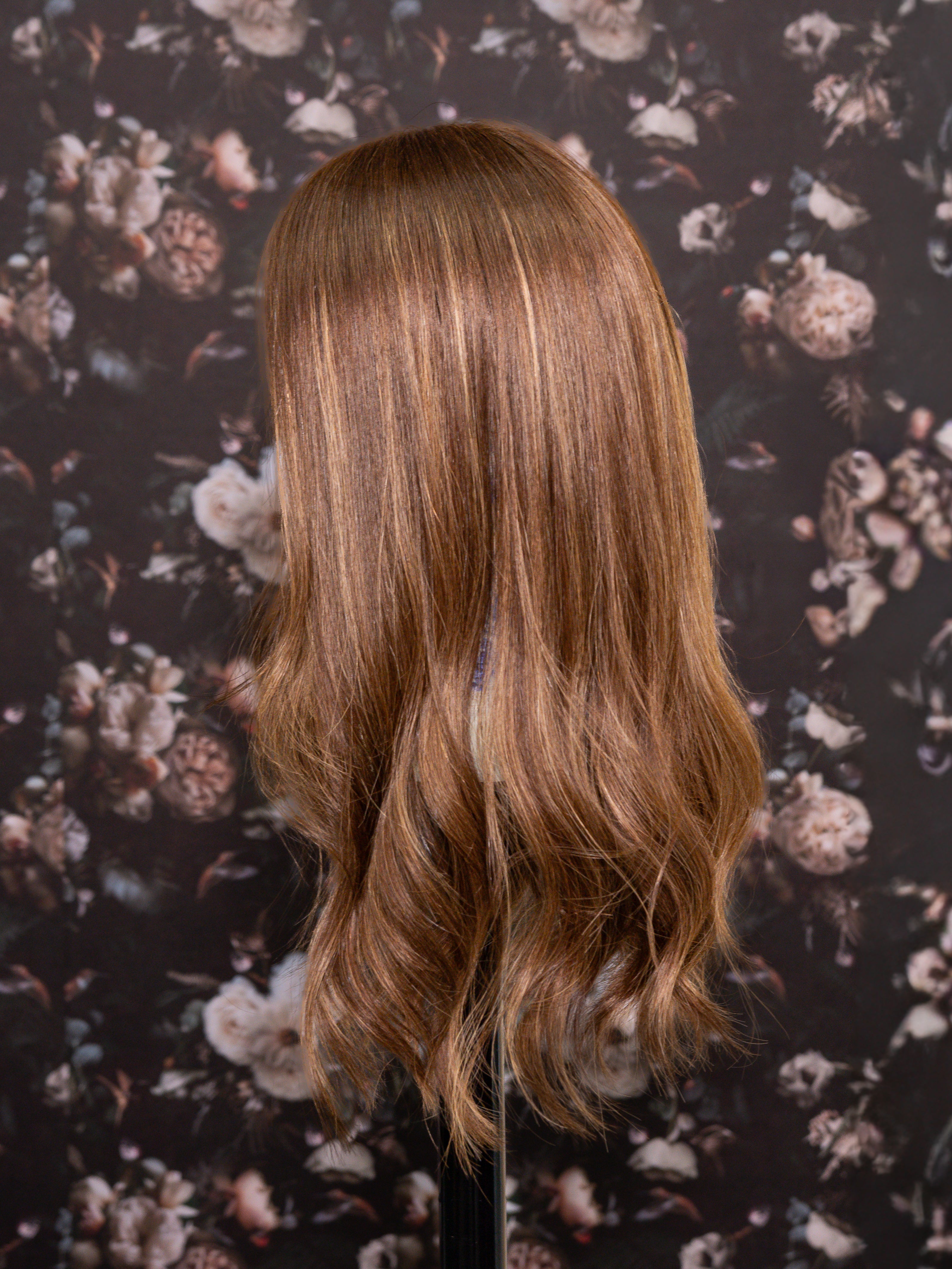 Brown wig on a mannequin head against a floral patterned background