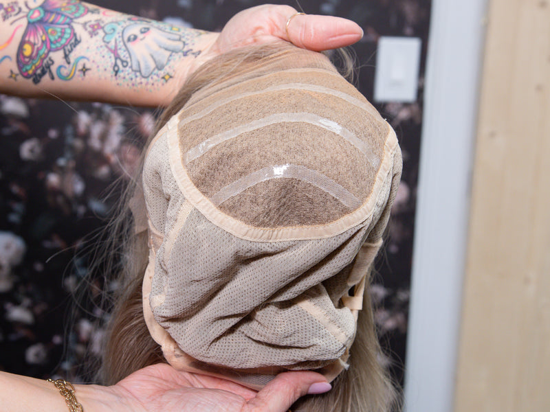 Person holding a wig cap with hair extensions inside, against a blurred background.
