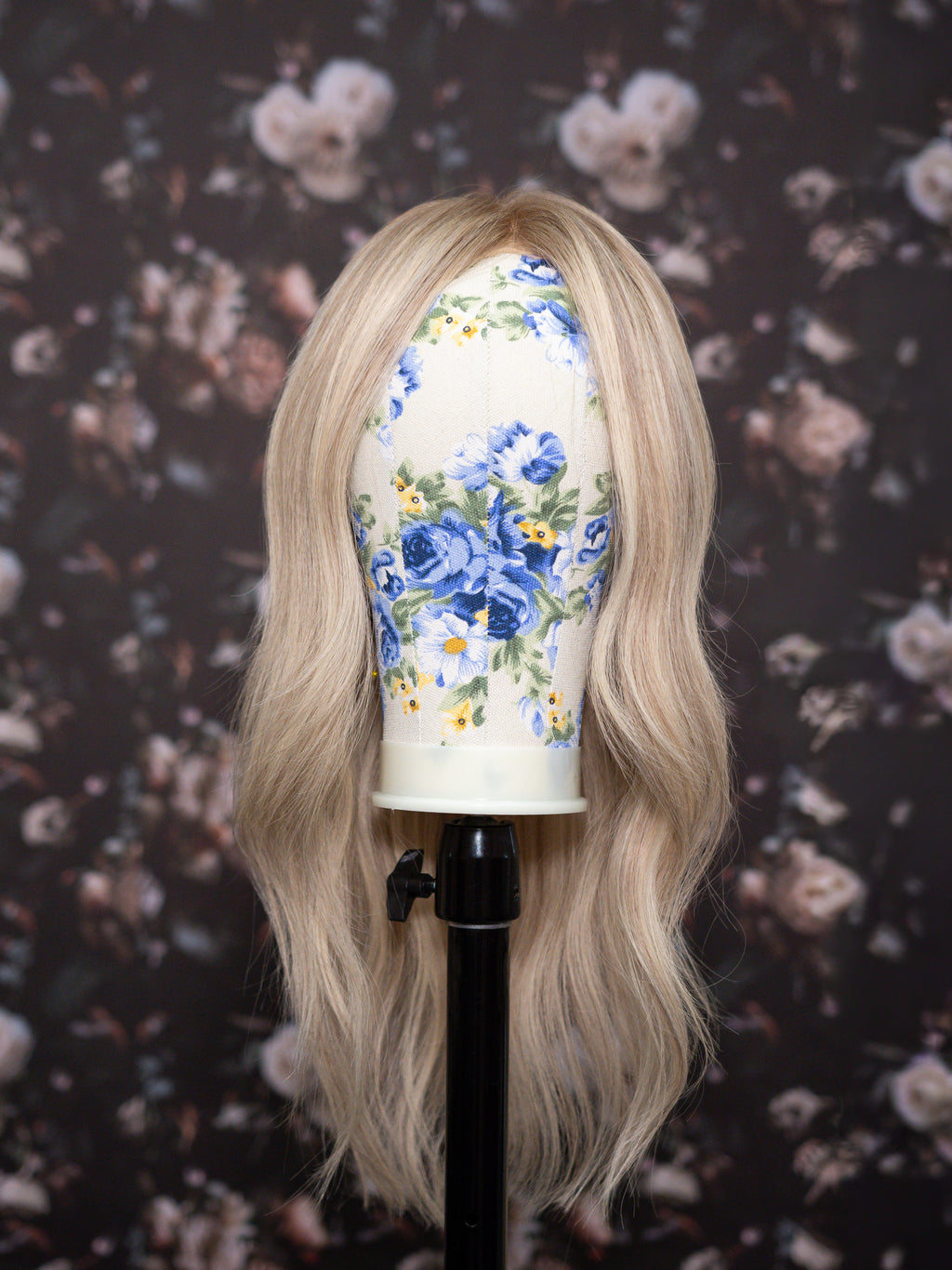 Blonde wig on a mannequin head with floral design against a floral-patterned background