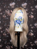 Blonde wig on a mannequin head with floral design against a floral-patterned background