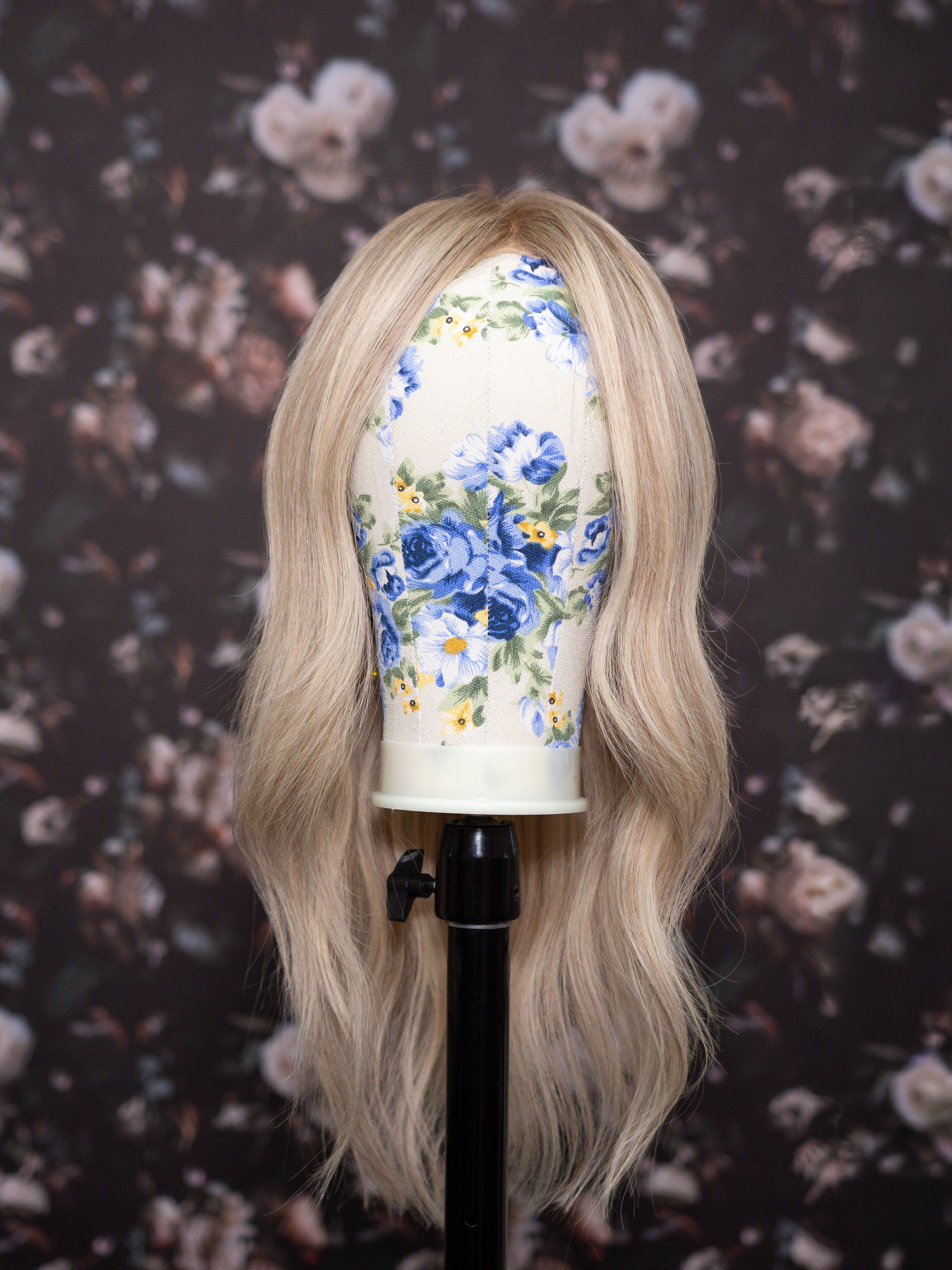 Blonde wig on a mannequin head with floral design against a floral-patterned background