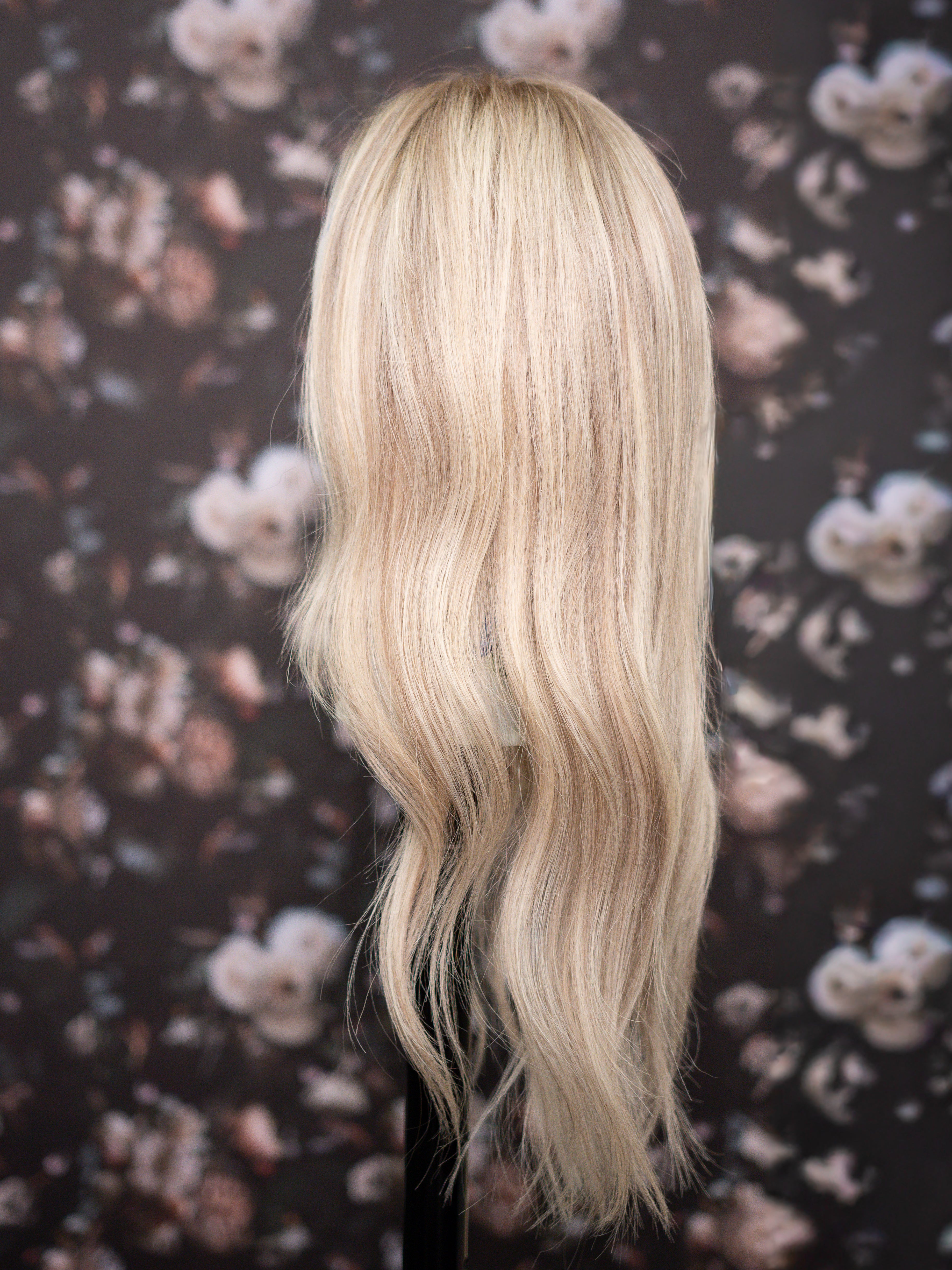 Blonde wig on a mannequin head against a floral patterned background