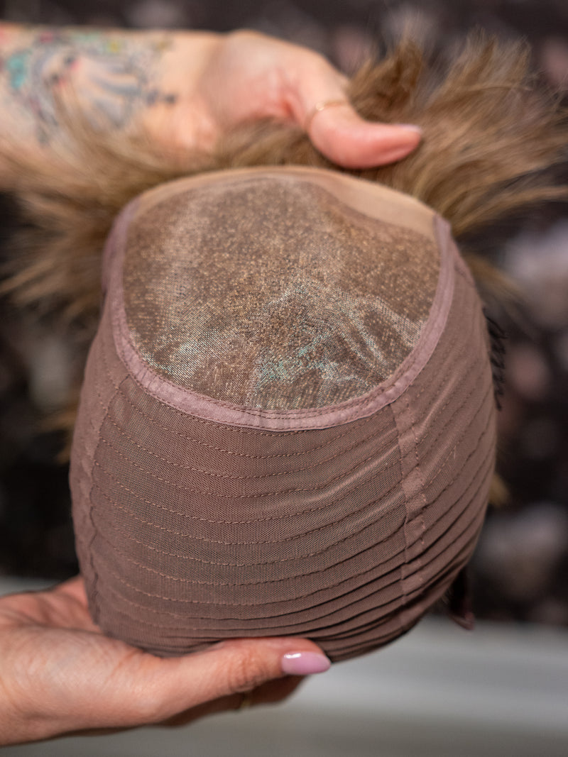 Close-up of a hairpiece held by a person with visible tattoos.
