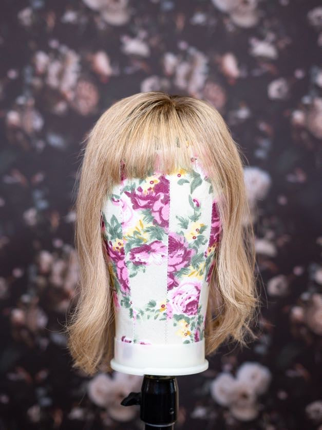 Blonde wig on a mannequin head with floral pattern against a dark background