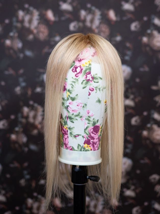 Blonde wig on a floral-patterned mannequin head against a dark floral background
