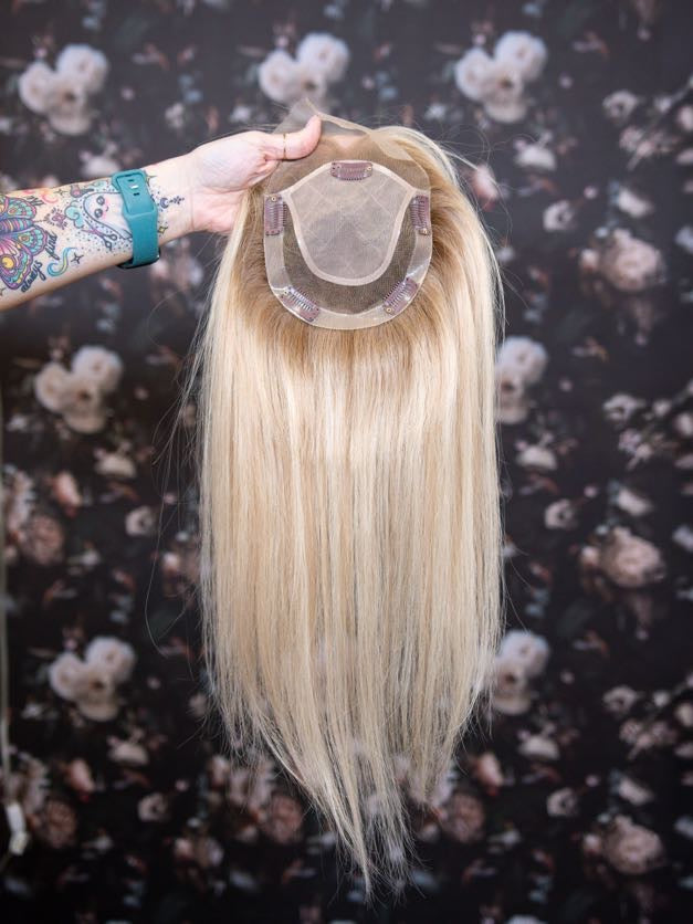 Blonde hair extension held by a hand against a floral background