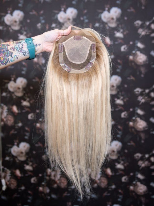 Blonde hair extension held by a hand against a floral background