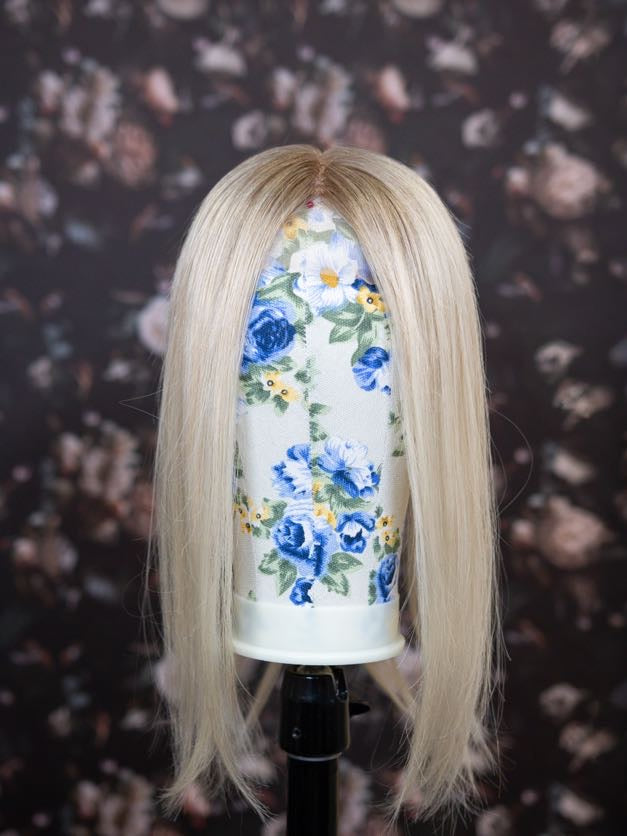 Blonde wig on a mannequin head with a floral-patterned container against a floral background