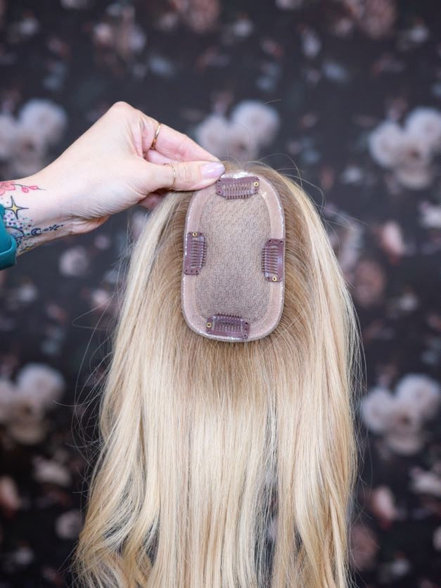 Blonde hair extension being held by a hand against a floral background