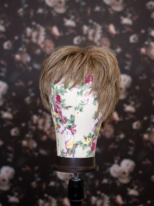 Mannequin head with brown hair styled on a floral-patterned stand against a dark floral background