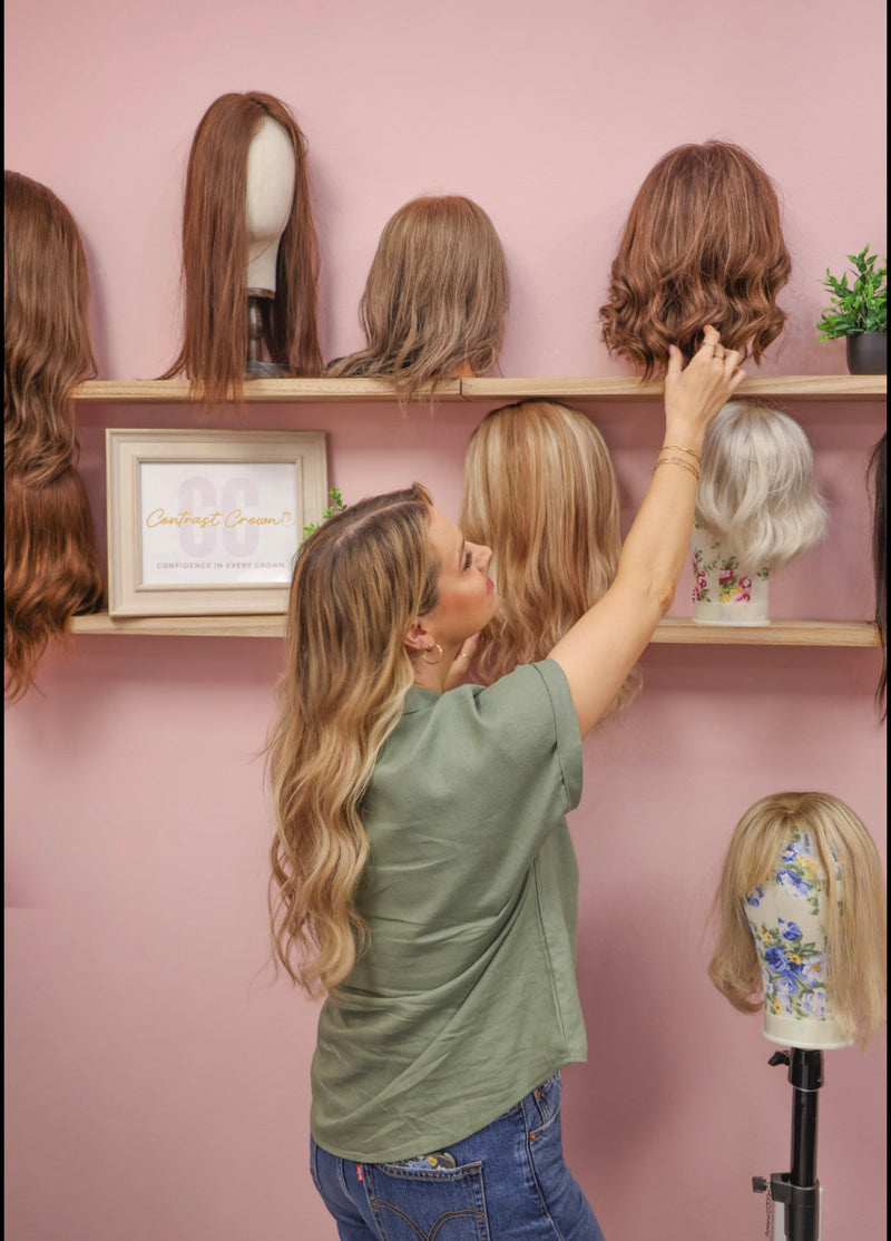Woman selecting a wig from a display against a pink wall