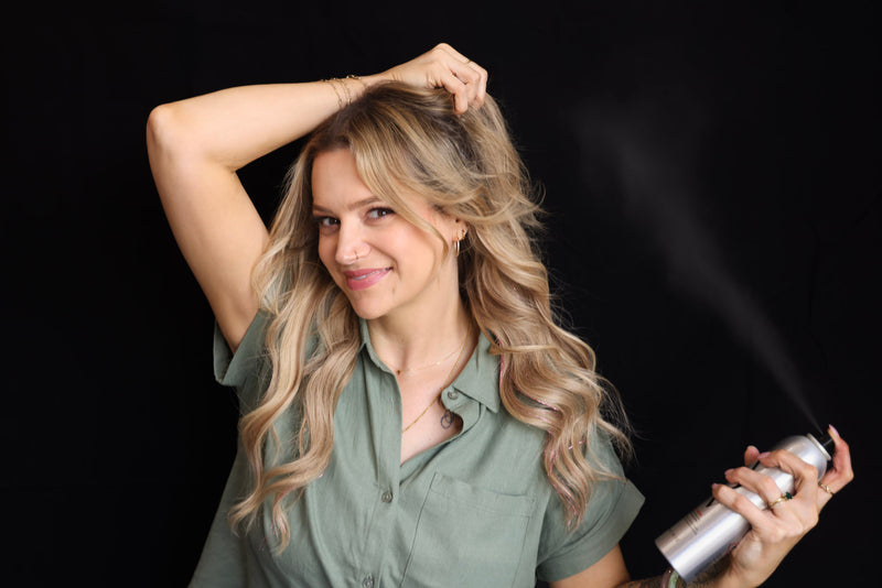 Woman with styled hair holding a hair product against a black background